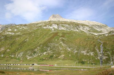 Einfahrt eines Zuges aus Andermatt kommend am Oberalpsee unmittelbar vor Einfahrt in den Bahnhof auf der Passhöhe
