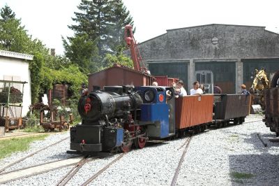 Die Feldbahnlok quert hier mit zwei Waldbahn-Personenwagen das Gleisvorfeld der Museumshalle. Die ungewöhnlichen Proportionen der Lok lassen eher den Eindruck einer Gartenbahn, gezogen von einem Modell eines normalspurigen B-Kupplers aufkommen.
Schlüsselwörter: Eisenbahnmuseum Schwechat , VEF , Feldbahn