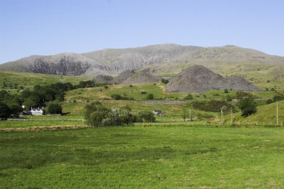 Die Westflanke des Snowdon, des höchsten Gipfels von England und Wales. Die Schutthalden in Bildmitte stammen von einigen kleineren Schieferminen, die hier einst für Fracht für die Bahn sorgten. Die Bahntrasse verläuft auf dem steinernen Damm davor. 
Schlüsselwörter: Welsh Highland Railway, Snowdon